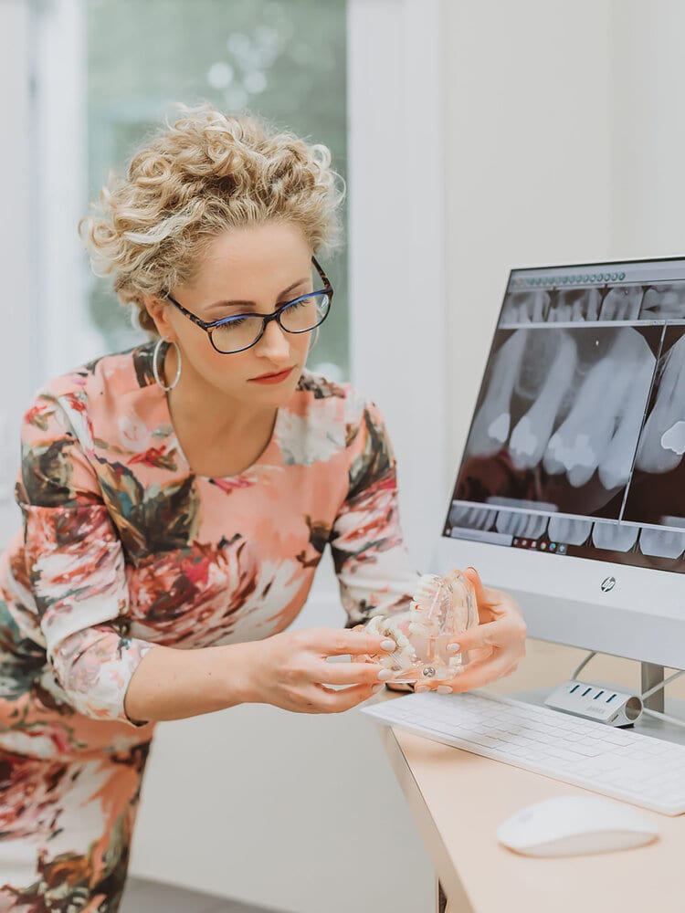 Dr. Inna Vinnikov reading dental X-rays on a monitor, holding a dental model