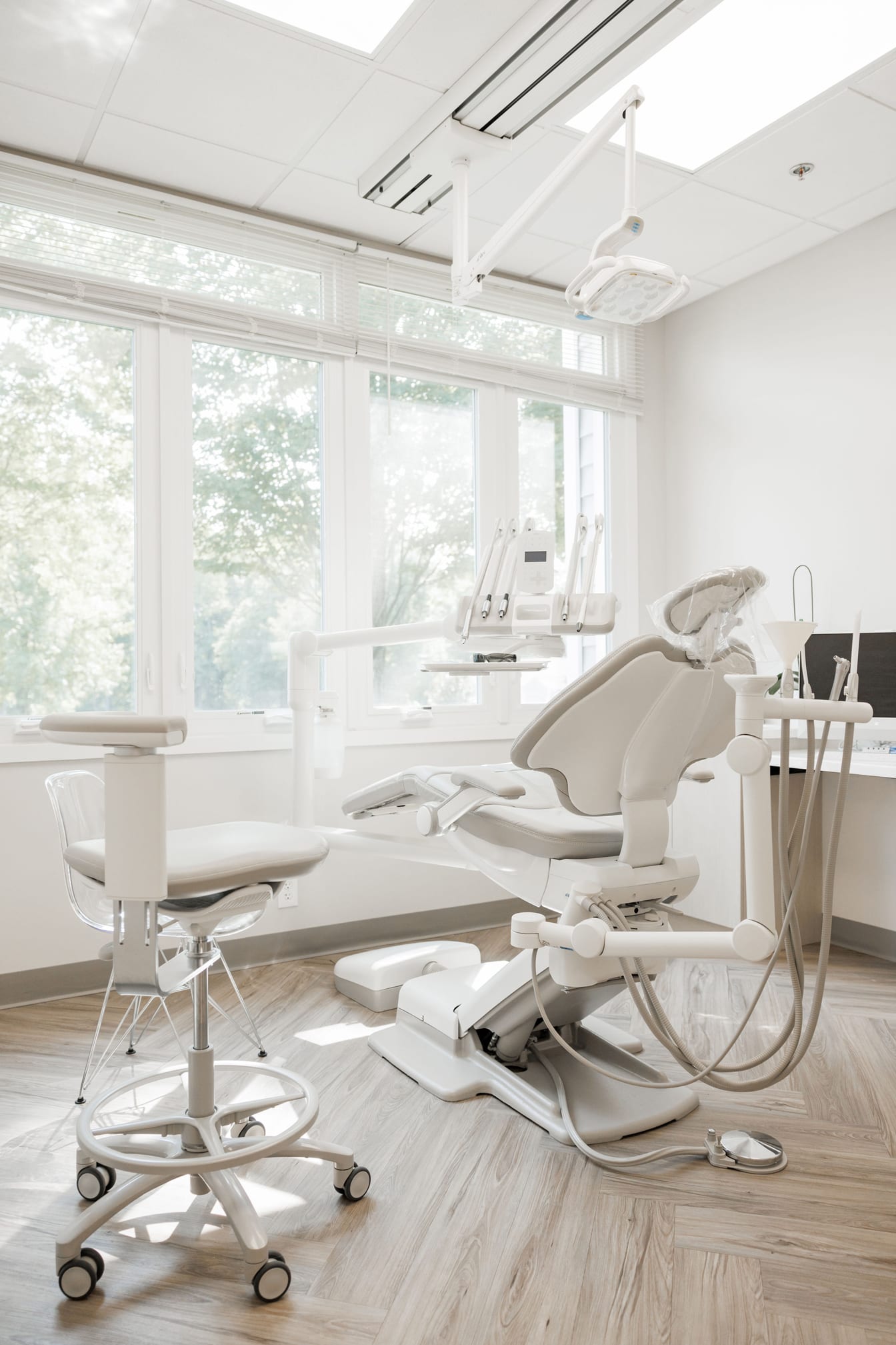 Treatment room at Inna Vinnikov, DMD: white dental chair, large windows looking out at trees